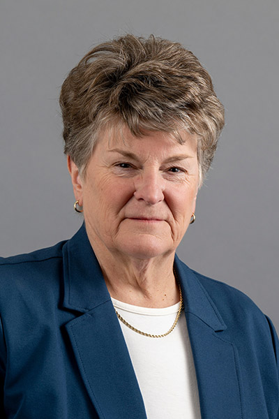 Portrait of woman with short, light brown hair, wearing a blue blazer, white top, and a thin gold necklace.